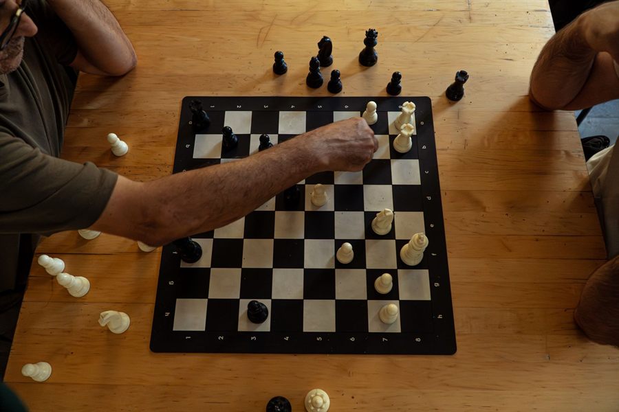 Overhead view of a hand moving a piece on a black-and-white chessboard on a wooden table