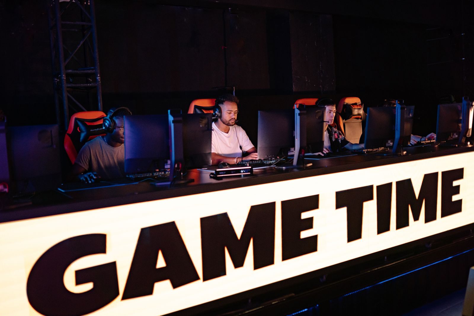Gamers in headsets at a row of computers behind a lit Game Time banner at an esports event