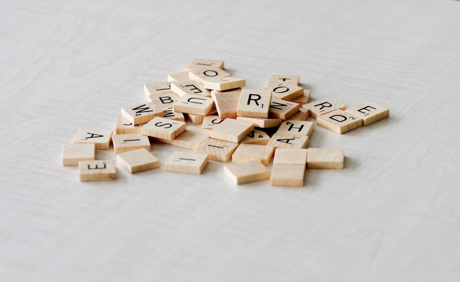 A small pile of wooden letter tiles on a pale table, the pieces used in a Scrabble tournament