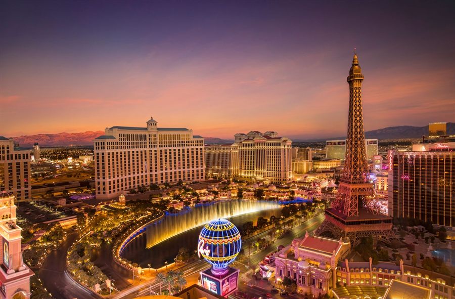 Las Vegas at dusk from above, with the Bellagio fountains lit and the Eiffel Tower replica of Paris Las Vegas